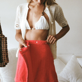 KABE SHOP INC Dolce skirt in bright red worn by a woman with a white crochet cardigan and bikini top