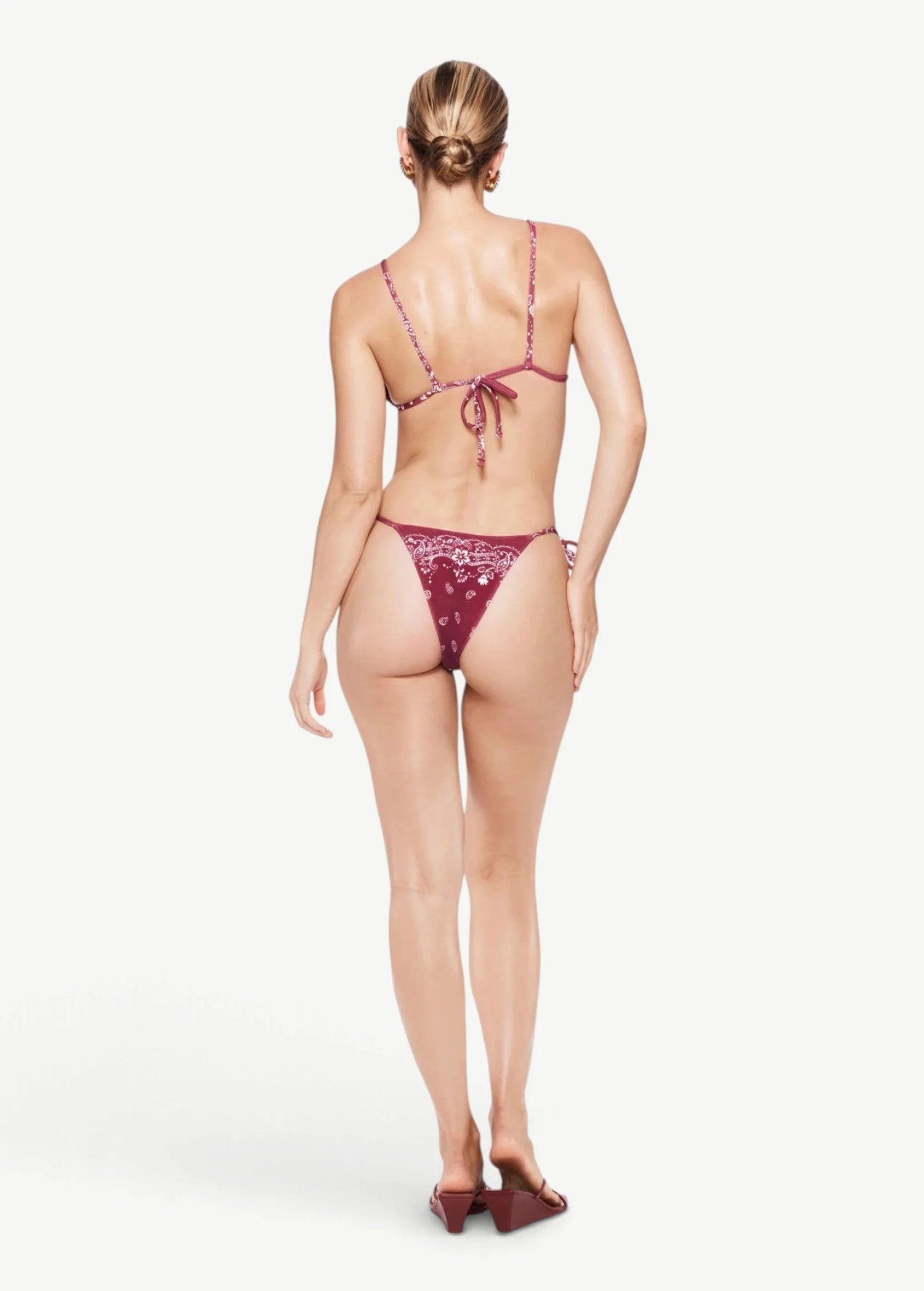 Model wearing KABE SHOP INC Equator triangle bikini top and matching bottom in burgundy paisley print from behind.