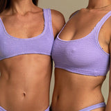 Two models wearing KABE SHOP INC Ginny bikini tops in textured lavender fabric with a sporty scoop neck silhouette.