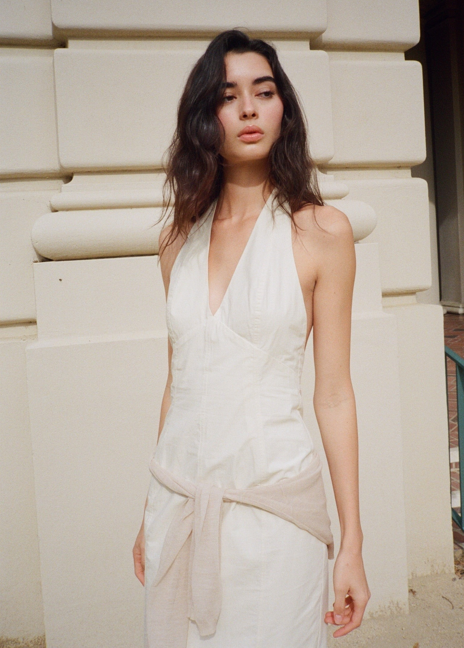 KABE SHOP INC Helia white halter gown with a plunging neckline and open back worn by a model outdoors