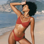 KABE SHOP INC Infinity Top in rust red with a front twist detail, worn by a model on a sunny beach.