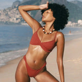 KABE SHOP INC Infinity Top in rust red with a front twist detail, worn by a model on a sunny beach.