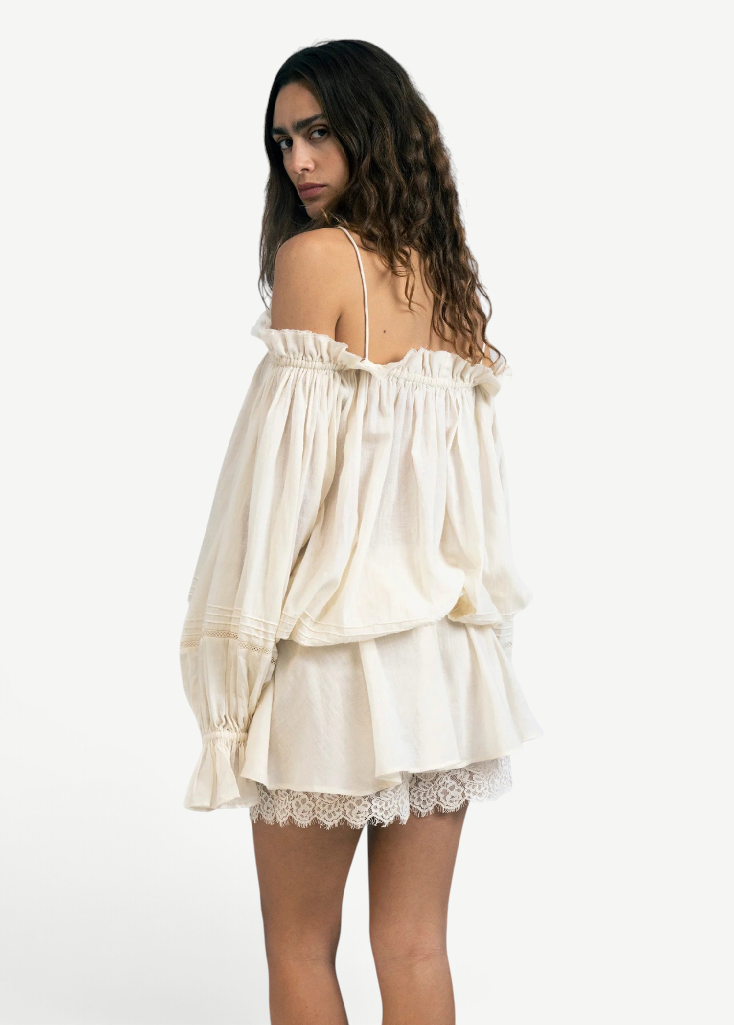 Model wearing a KABE SHOP INC Isabella jumpsuit in cream cotton with off-the-shoulder sleeves and delicate lace trim.
