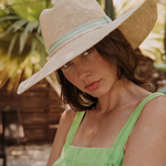 KABE SHOP INC Isabella wide brim straw hat with a light green striped ribbon, worn by a woman in a sunny garden.