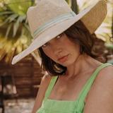 KABE SHOP INC Isabella wide brim straw hat with a light green striped ribbon, worn by a woman in a sunny garden.