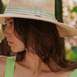 KABE SHOP INC Isabella wide brim straw hat with a striped ribbon detail worn by a woman in a sunny outdoor setting