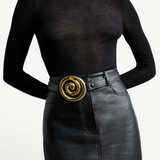 KABE SHOP INC Koru belt in black Italian calfskin with a sculptural gold spiral buckle worn over a black skirt