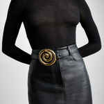 KABE SHOP INC Koru belt in black Italian calfskin with a sculptural gold spiral buckle worn over a black skirt