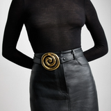 KABE SHOP INC Koru belt in black Italian calfskin with a sculptural gold spiral buckle worn over a black skirt