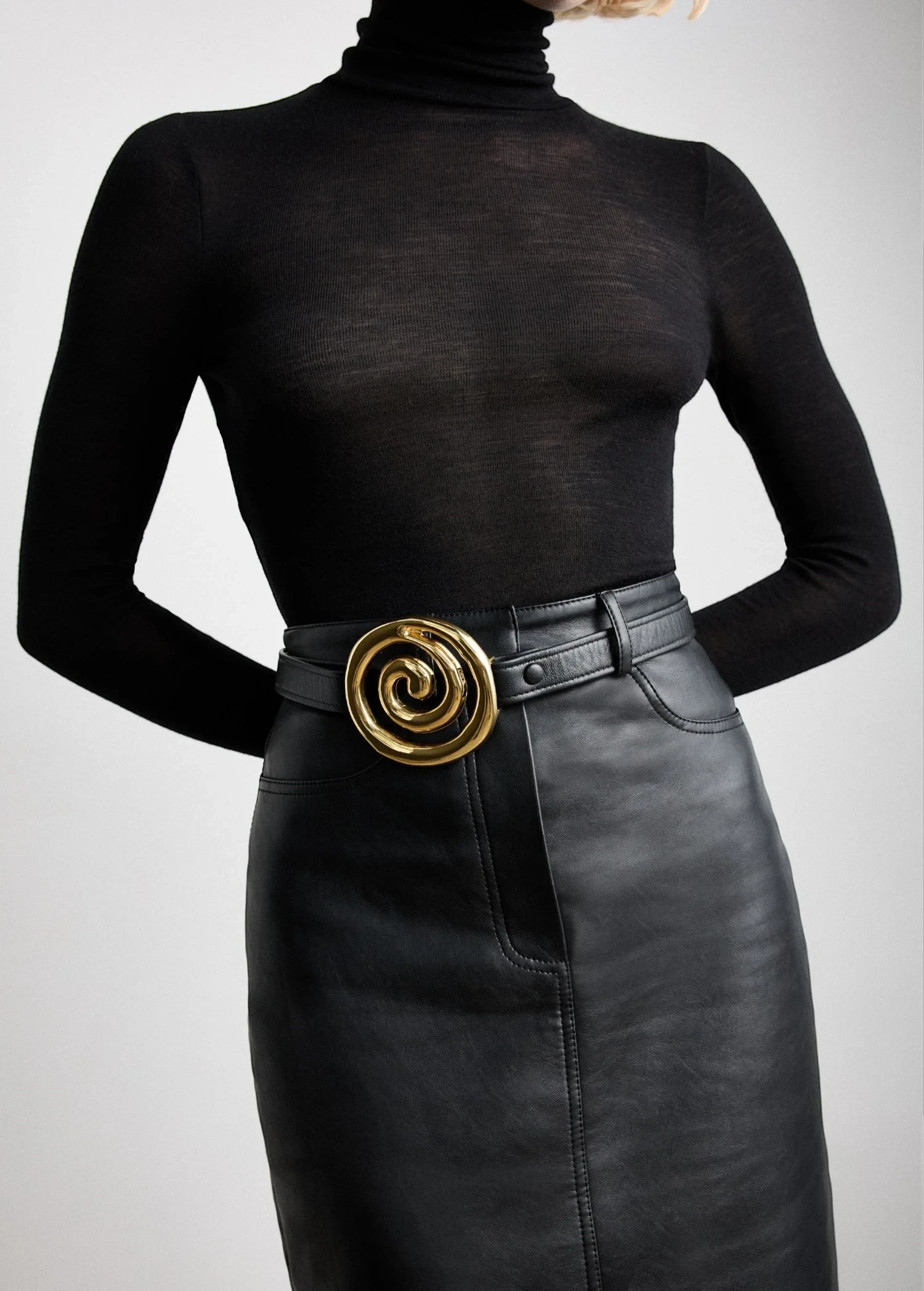 KABE SHOP INC Koru belt in black Italian calfskin with a sculptural gold spiral buckle worn over a black skirt