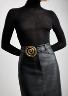 KABE SHOP INC Koru belt in black Italian calfskin with a sculptural gold spiral buckle worn over a black skirt