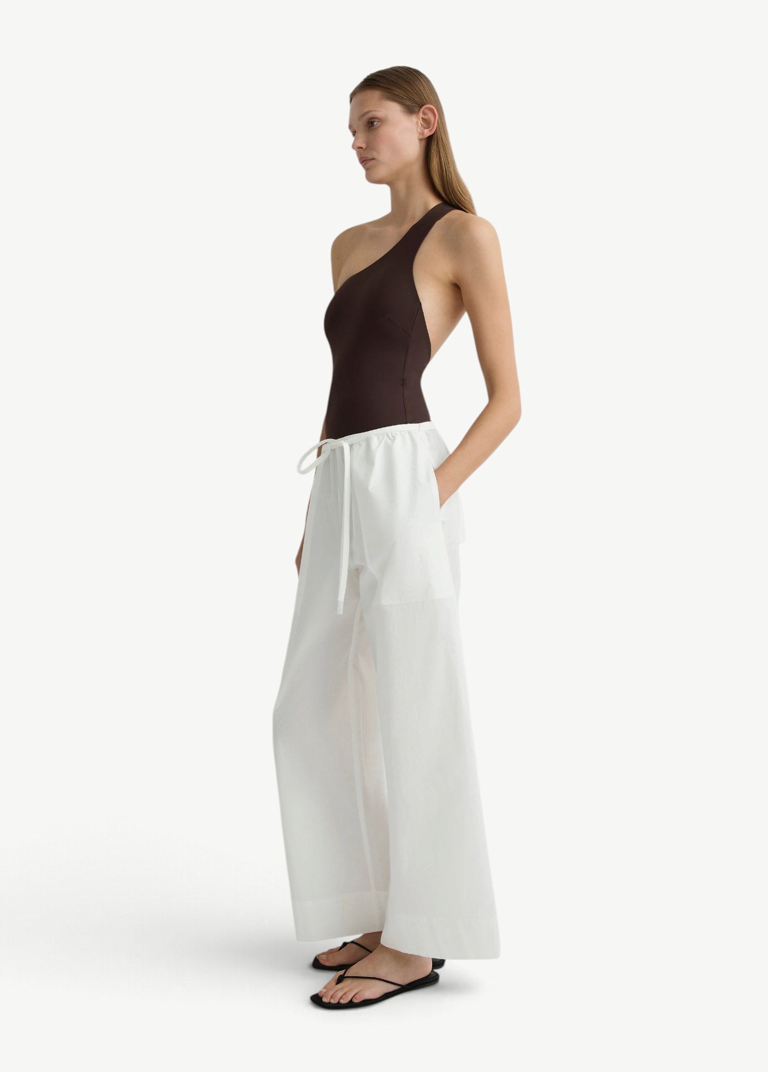 Model wearing KABE SHOP INC white Kyoto wide leg cotton pants with a brown one-shoulder bodysuit and black sandals.