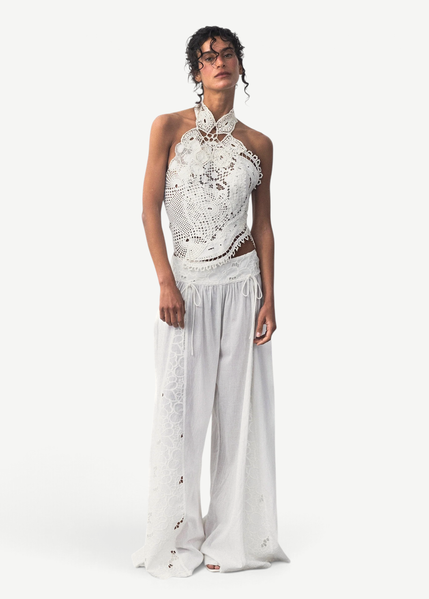 Model wearing KABE SHOP INC Menorca trousers in white cotton with intricate lace detailing and a relaxed fit.