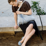 KABE SHOP INC Deiji Studios metallic knit chain bag with drawstring pouch worn by a woman sitting on a stone bench