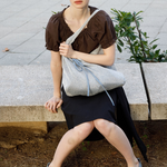 Model sitting on a stone bench wearing a KABE SHOP INC Deiji Studios metallic knit chain bag with a drawstring pouch.
