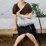 Model sitting on a stone bench wearing a KABE SHOP INC Deiji Studios metallic knit chain bag with a drawstring pouch.