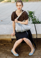 Model sitting on a stone bench wearing a KABE SHOP INC Deiji Studios metallic knit chain bag with a drawstring pouch.