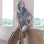 Model wearing KABE SHOP INC Nera wide leg pants with a tribal ikat print in brown and cream on a sunny terrace.