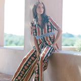 Model wearing KABE SHOP INC Nera wide leg pants with a tribal ikat print in brown and cream on a sunny terrace.