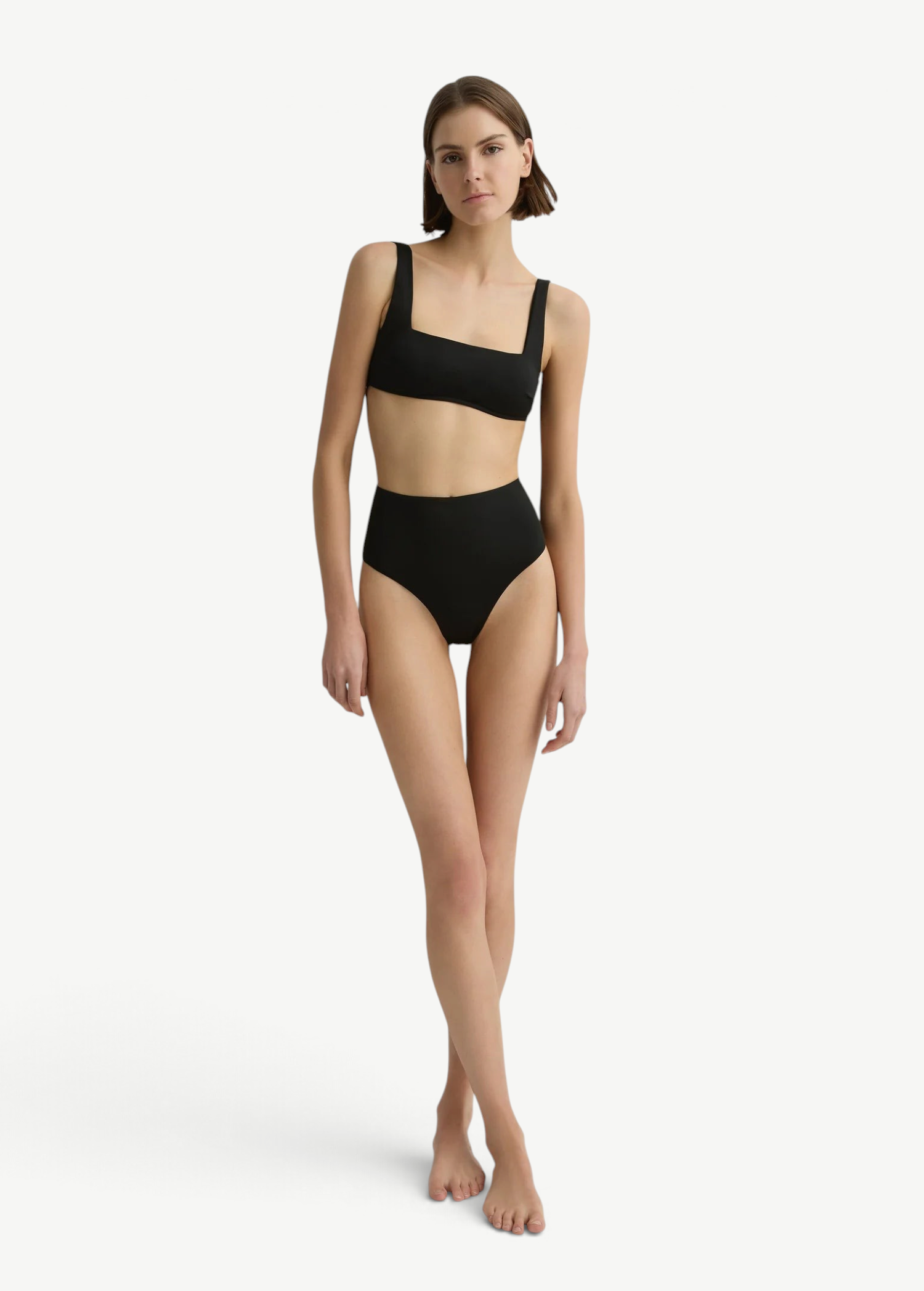 Model wearing KABE SHOP INC Poppy high-waisted black bikini bottoms and matching crop top against a white wall.