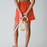 A model from KABE SHOP INC wears a red Terry Dolce skirt, white bikini top, and woven sandals, back view.