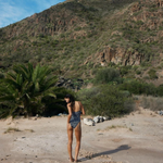 KABE SHOP INC Regatta One Piece swimsuit with zig-zag pattern worn by a woman on a sunny beach with mountain backdrop