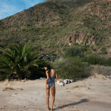 KABE SHOP INC Regatta One Piece swimsuit with zig-zag pattern worn by a woman on a sunny beach with mountain backdrop