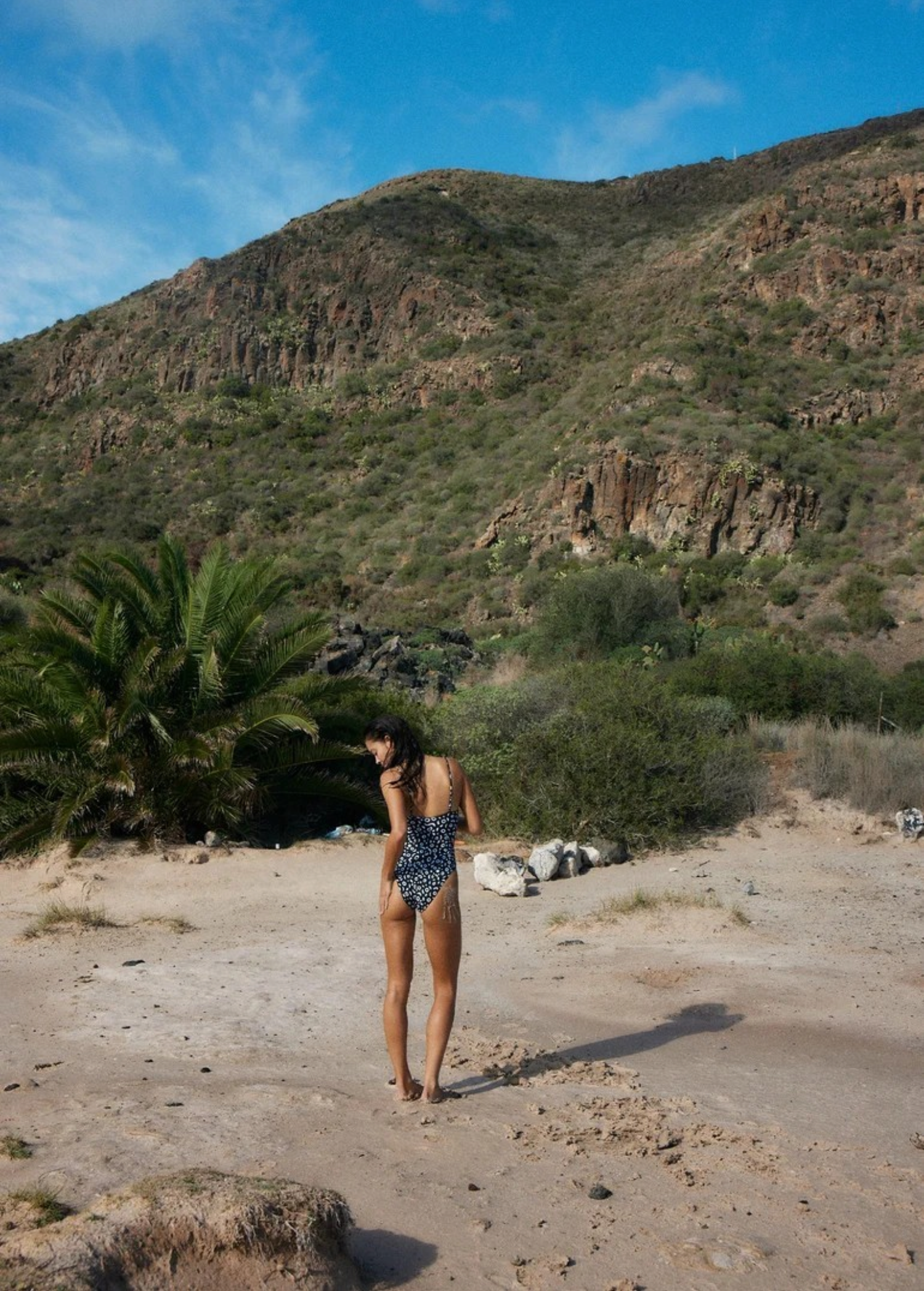 KABE SHOP INC Regatta One Piece swimsuit with zig-zag pattern worn by a woman on a sunny beach with mountain backdrop