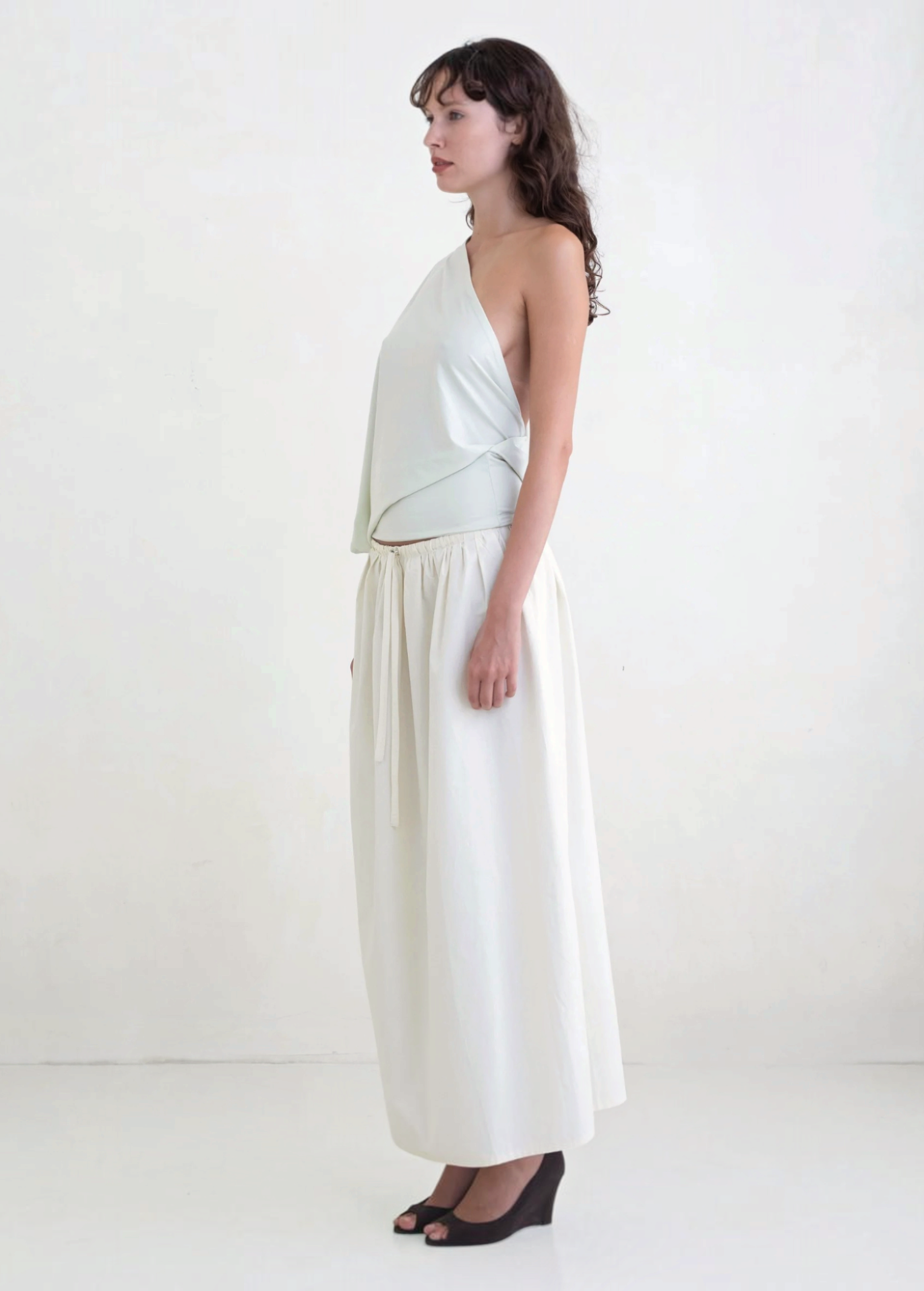 Model wearing a KABE SHOP INC Rhea maxi skirt in white with an adjustable drawstring waistband, side profile view.