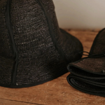 KABE SHOP INC Sandra foldable black straw hat with a classic silhouette, shown open and folded on a wooden surface.