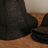 KABE SHOP INC Sandra foldable black straw hat with a classic silhouette, shown open and folded on a wooden surface.
