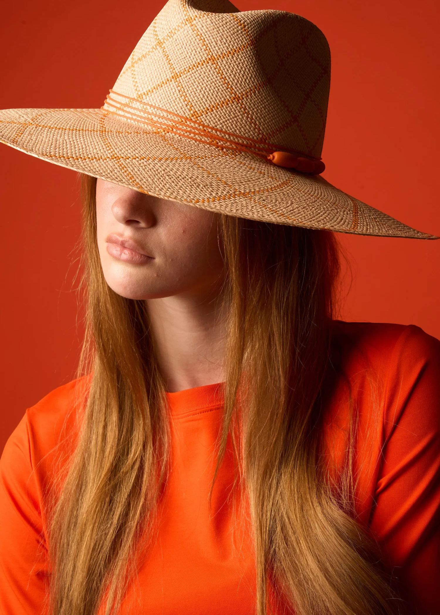 KABE SHOP INC Sangay wide brim straw hat with orange grid pattern worn by a model against a vibrant orange background
