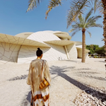 KABE SHOP INC The Sharis Kimono in beige and brown tie-dye worn by a woman with a bun, standing near modern architecture