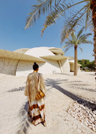 KABE SHOP INC The Sharis Kimono in beige and brown tie-dye worn by a woman with a bun, standing near modern architecture