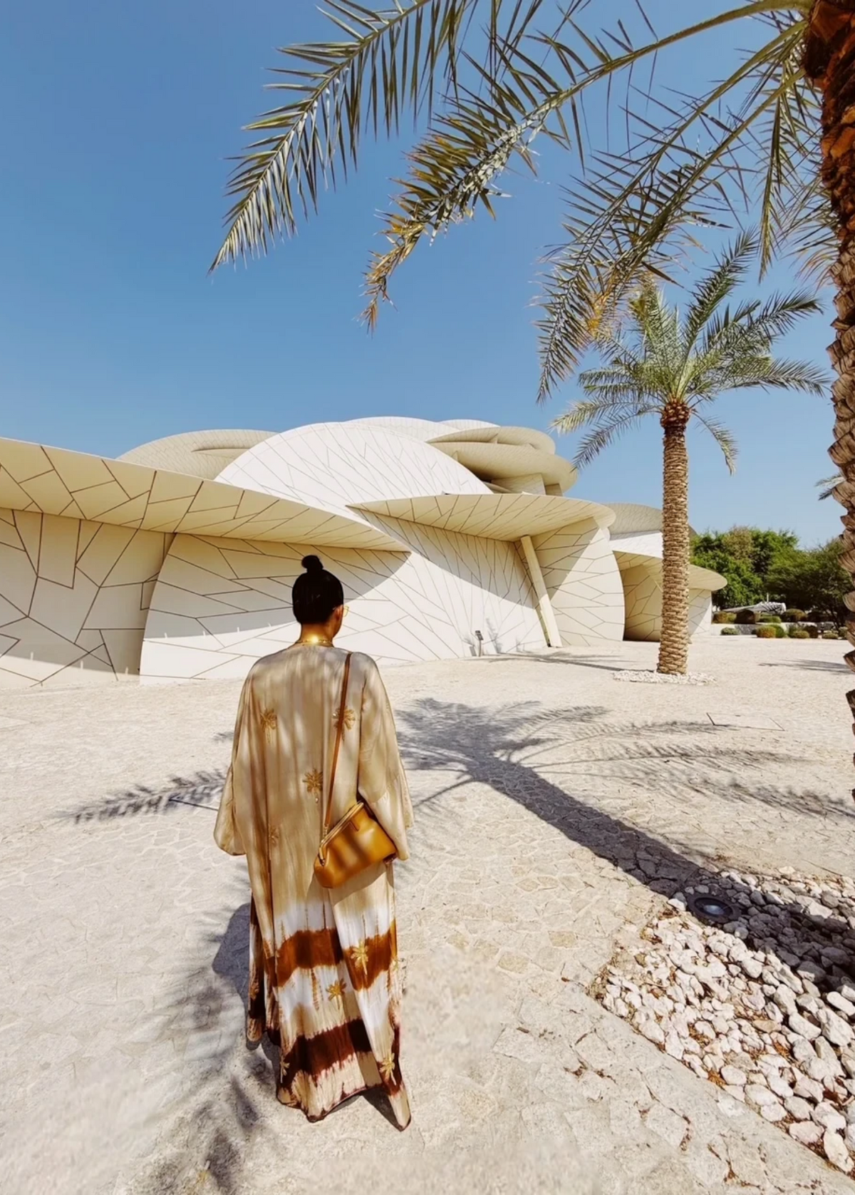 KABE SHOP INC The Sharis Kimono in beige and brown tie-dye worn by a woman with a bun, standing near modern architecture