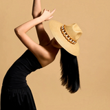 KABE SHOP INC Sine wide brim straw hat with wooden bead detail worn by a model in a black dress against a tan background