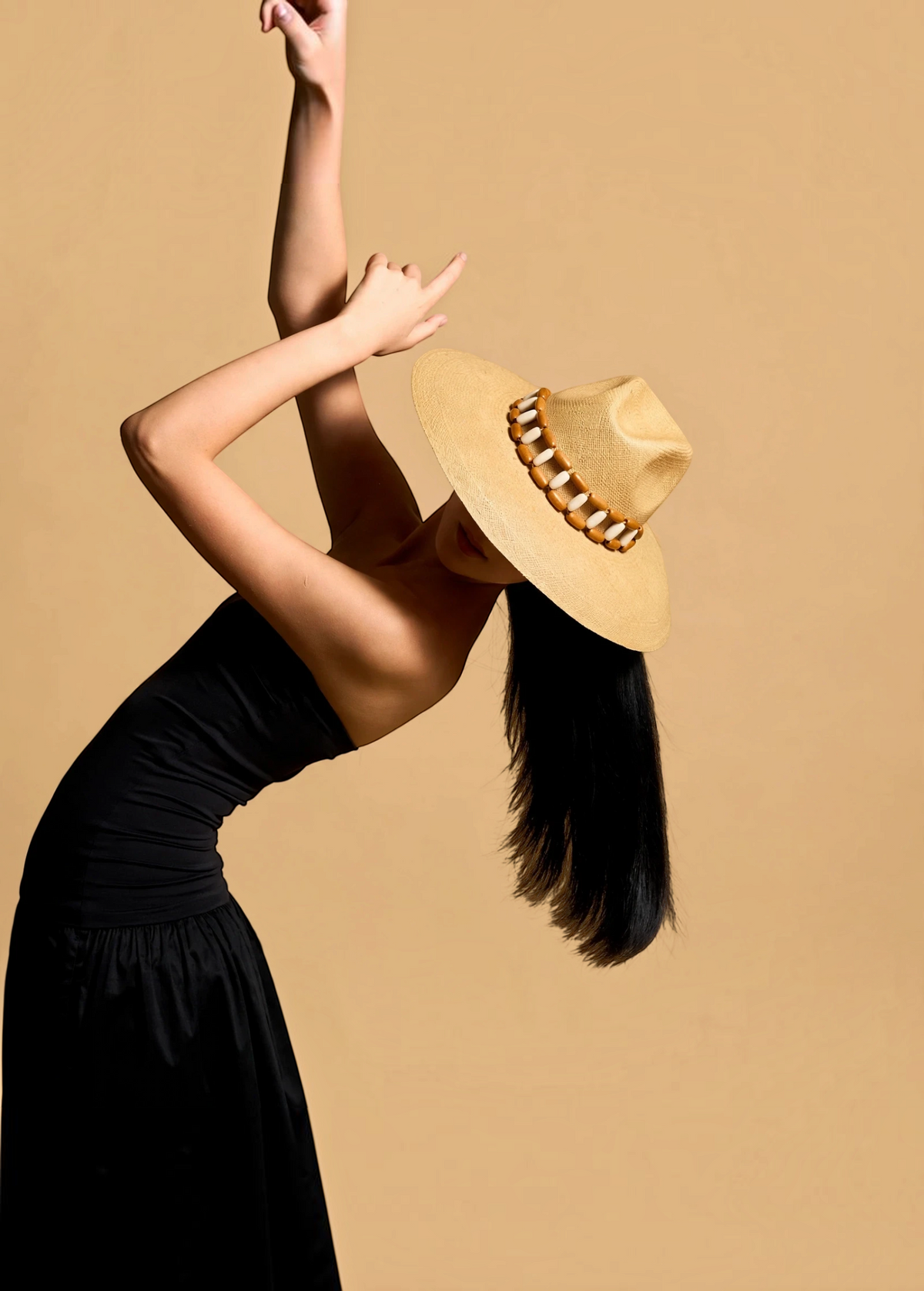 KABE SHOP INC Sine wide brim straw hat with wooden bead detail worn by a model in a black dress against a tan background