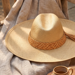 KABE SHOP INC Tucan wide brim straw hat with a woven leather band and tassel detail resting on a linen cloth.