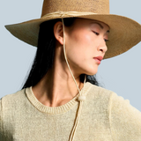 Model wearing a KABE SHOP INC Vitoria wide brim straw hat with a chin strap against a blue background