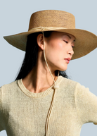 Model wearing a KABE SHOP INC Vitoria wide brim straw hat with a chin strap against a blue background