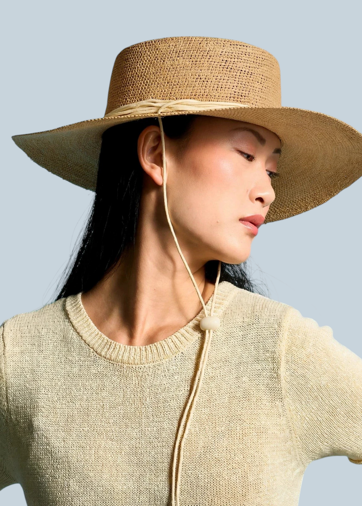 Model wearing a KABE SHOP INC Vitoria wide brim straw hat with a chin strap against a blue background
