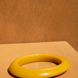 KABE SHOP INC yellow resin bangle bracelet with a smooth, sculptural design on a warm-toned surface