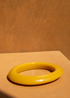 KABE SHOP INC yellow resin bangle bracelet with a smooth, sculptural design on a warm-toned surface