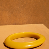 KABE SHOP INC yellow resin bangle bracelet with a smooth, sculptural design on a warm-toned surface