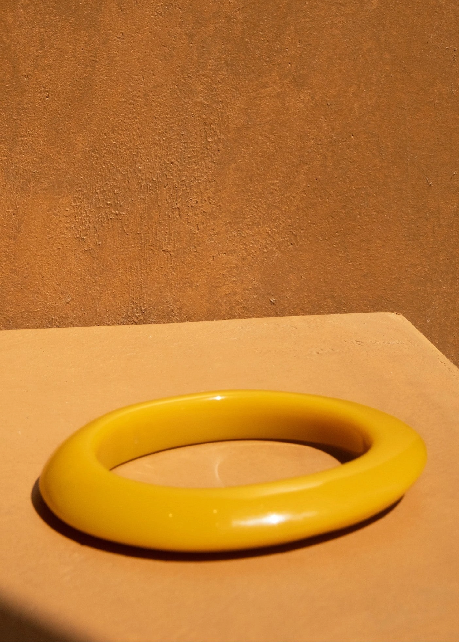KABE SHOP INC yellow resin bangle bracelet with a smooth, sculptural design on a warm-toned surface