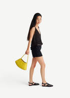 Model carrying a yellow handwoven Buffalo leather Rosanna Bag from KABE SHOP INC, featuring a sleek shoulder design.