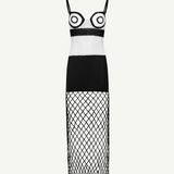 La Femme Dress: This black-and-white sleeveless dress features thin straps and bold circular patterns on the bodice, complemented by a solid black midsection. The skirt is crafted from crochet fabric with see-through diamond-patterned netting, creating an elegant yet modern look. Photographed against a plain white background.
