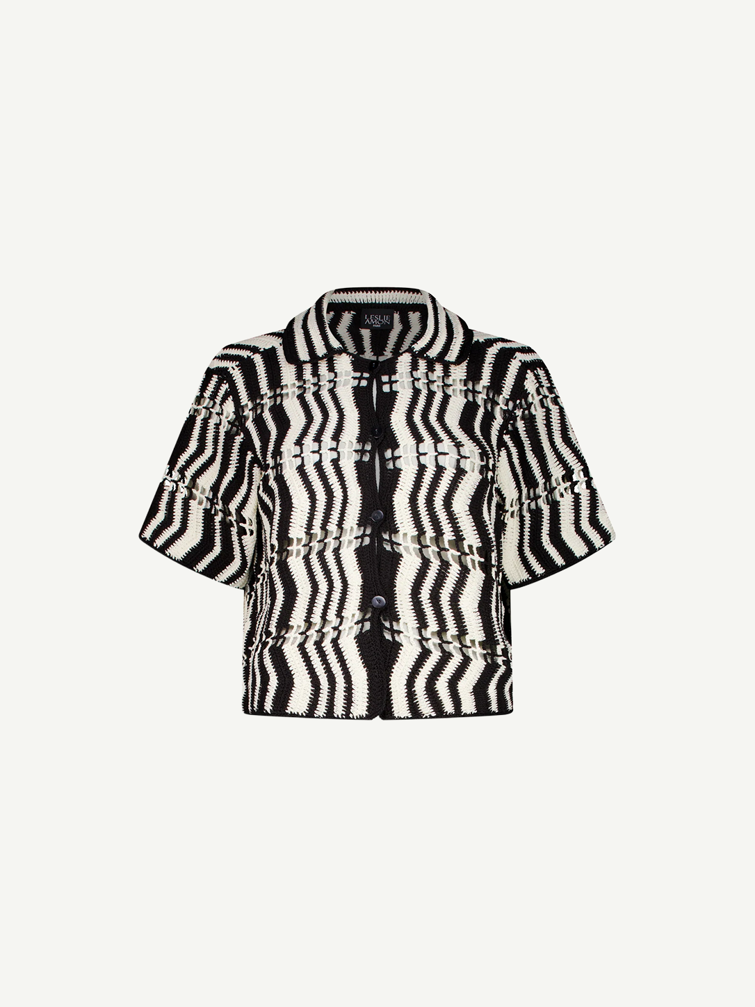 The Riviera Shirt is a black-and-white short-sleeve button-up summer shirt featuring a bold zigzag wavy pattern and a collar, displayed on a plain white background. This black-and-white crochet Riviera Shirt adds a unique textured twist to classic warm-weather style.