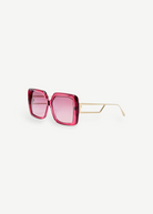 The Macy Sunglasses feature a square-shaped, oversized frame crafted from luxurious Italian acetate in bold pink, with light pink gradient lenses and elegant gold-plated temples and thin arms, showcased on a white background.