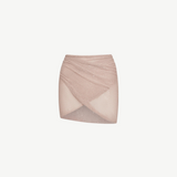 The Lumiere Skirt is a light pink, textured knit mini skirt with a criss-cross, wrap-style front and subtle sparkle details, featuring sequin bead accents for added shimmer, isolated on a white background.